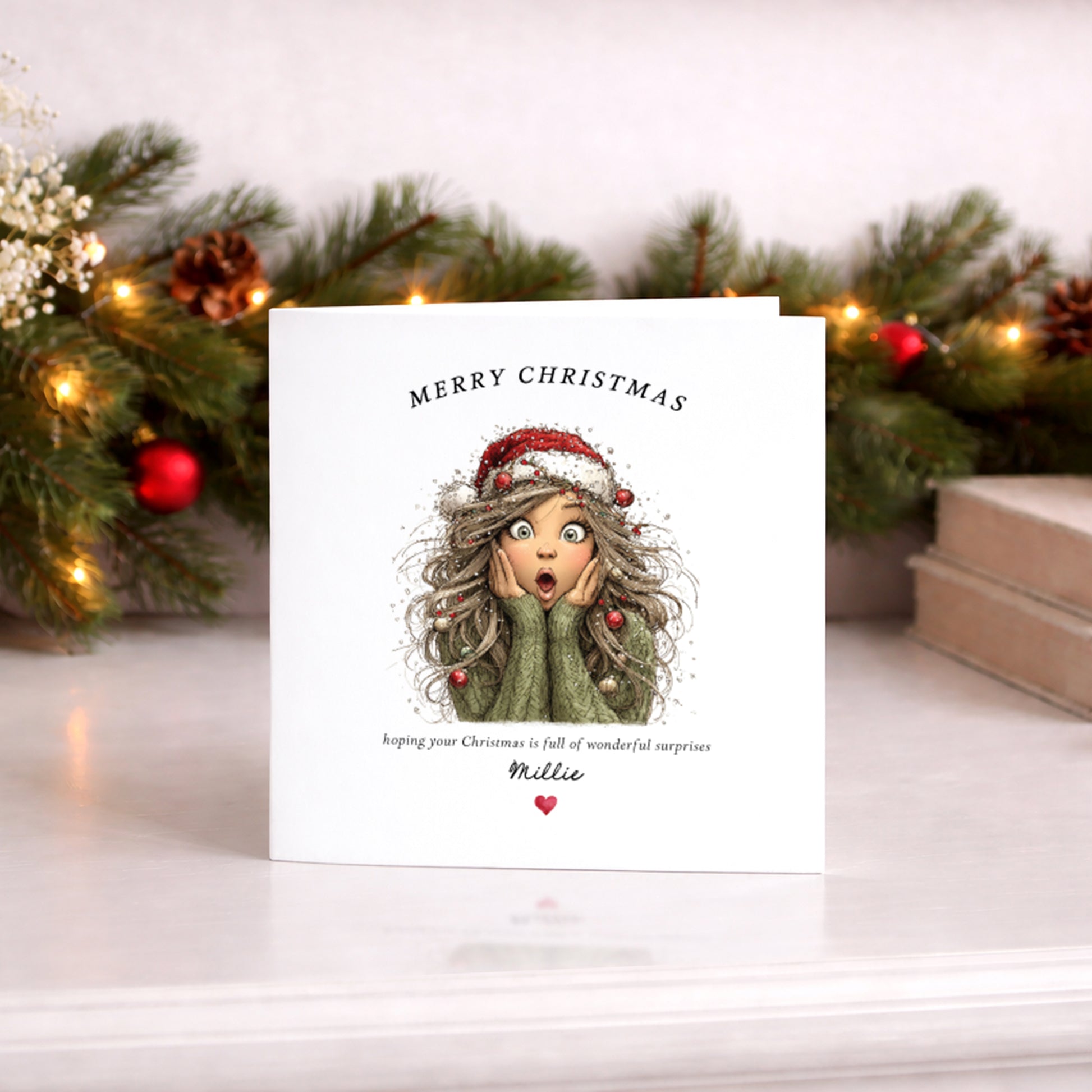 A personalized Christmas greeting card with an illustration of a surprised girl in a green sweater and Santa hat, standing on a white surface with a blurred festive background of pine branches and warm lights.