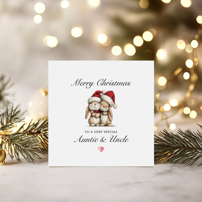 Christmas card with hugging bunnies wearing Santa hats with text "Merry Christmas to a very special Auntie & Uncle" on a decorative background