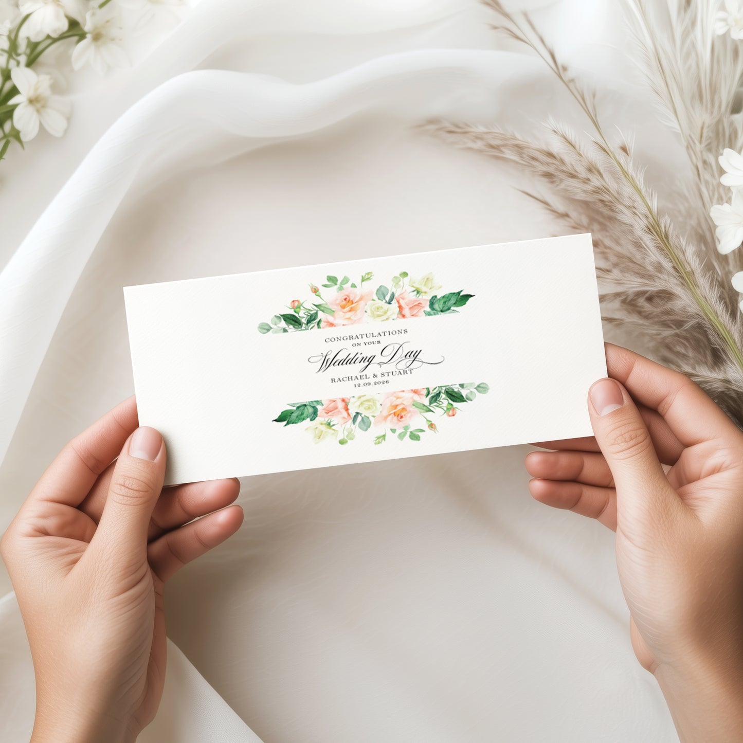 Hands holding a wedding money wallet card with peach floral design. The words on your wedding day with the couples names and wedding date on a soft fabric background