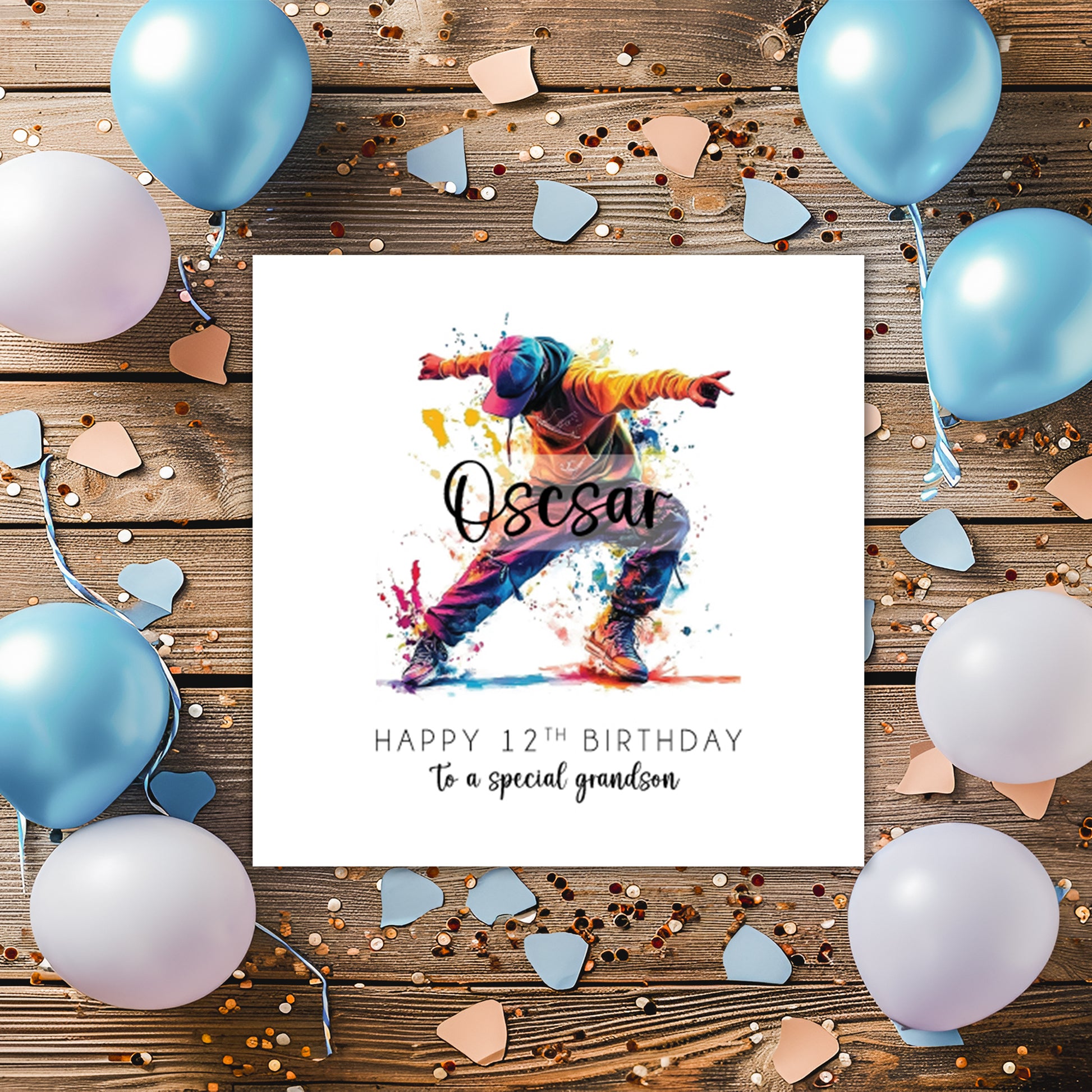 A square white birthday card featuring a vibrant watercolour illustration of a male street dancer mid-move, arms outstretched and legs wide apart, wearing an orange hoodie, blue cap, baggy jeans and trainers, surrounded by colourful paint splashes in yellow, pink, blue and red. The name "Oscar" is overlaid in bold cursive script across the illustration. Below, the text reads "Happy 12th Birthday" in spaced capitals, followed by "to a special grandson" in flowing script. The card is displayed on a wooden sur