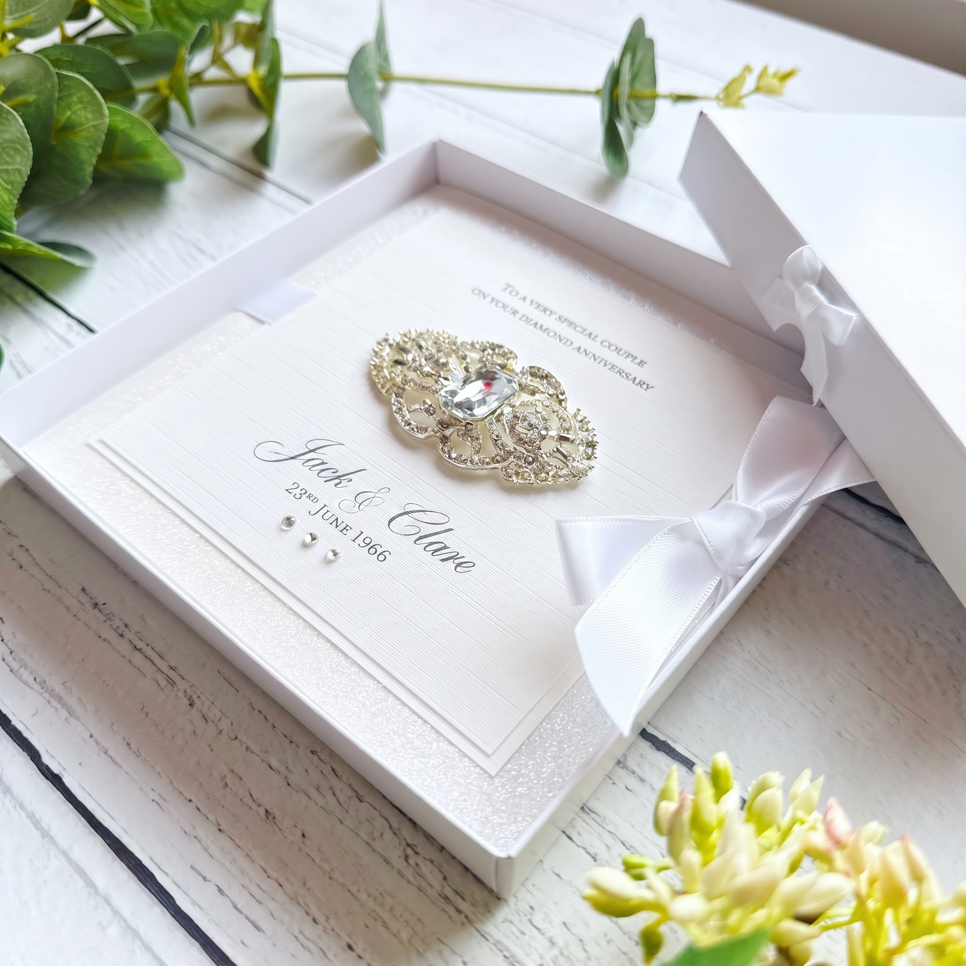 White diamond anniversary card with layers of white glitter. Featuring an art deco inspired rhinestone brooch. With personalised text. In a box.