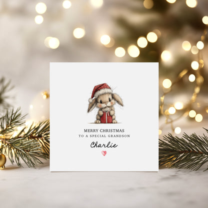 Christmas card with a bunny wearing a Santa hat and holding a gift with personalised text, surrounded by festive lights and greenery.