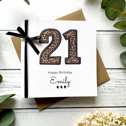 Leopard print '21' birthday card with a black ribbon on a white wooden surface.