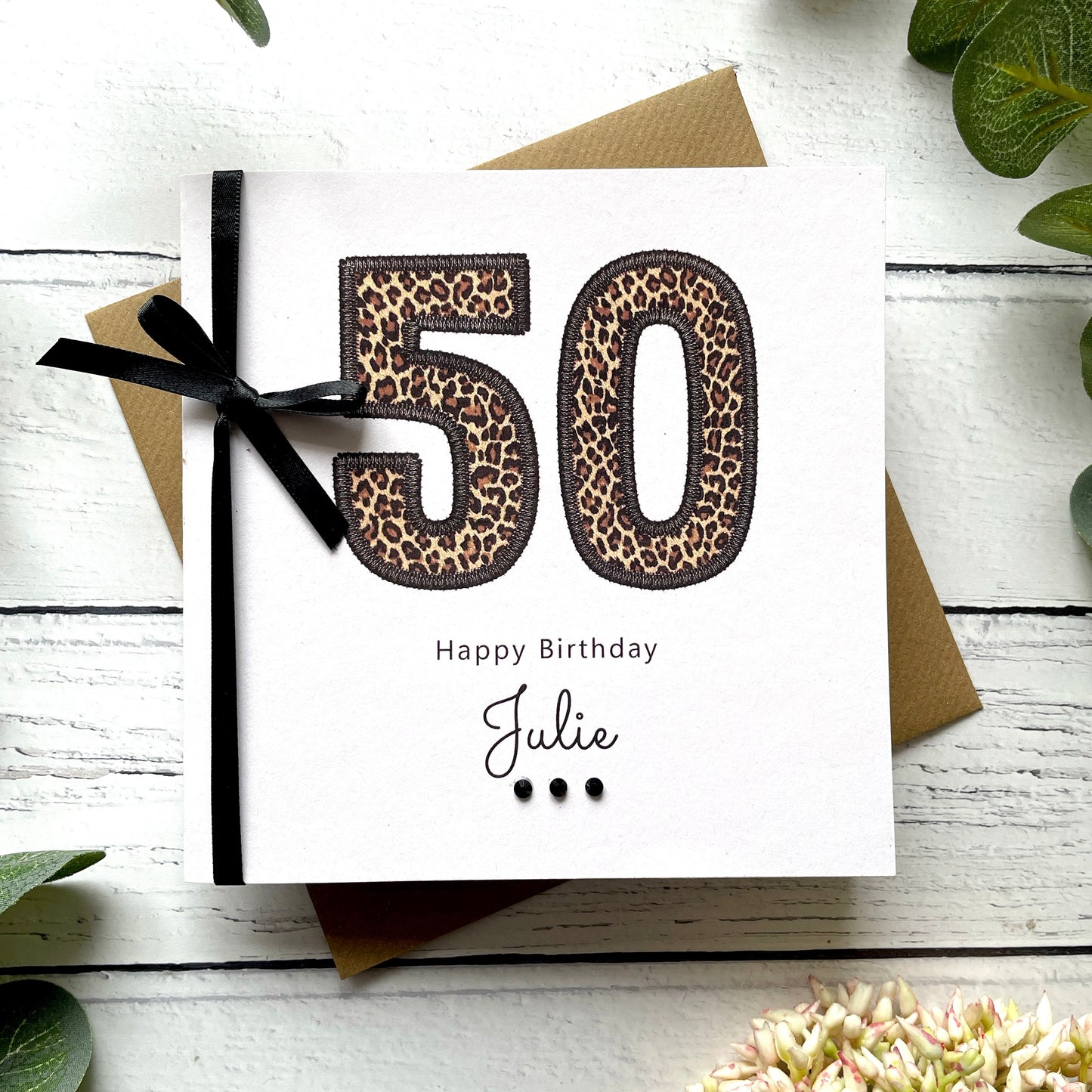 50th birthday card with leopard print numbers and a black bow on a white wooden surface.