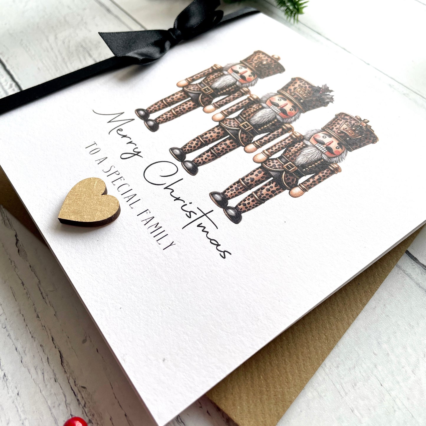 A white Christmas greeting card featuring three illustrated nutcracker figures and the text 'Merry Christmas to a special family,' styled on a light wood surface with a black ribbon and a small gold heart.