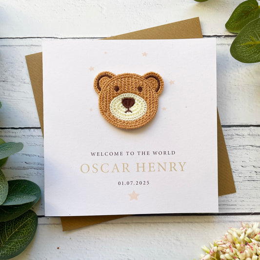 New baby card with teddy bear design and personalised text on a wooden surface.