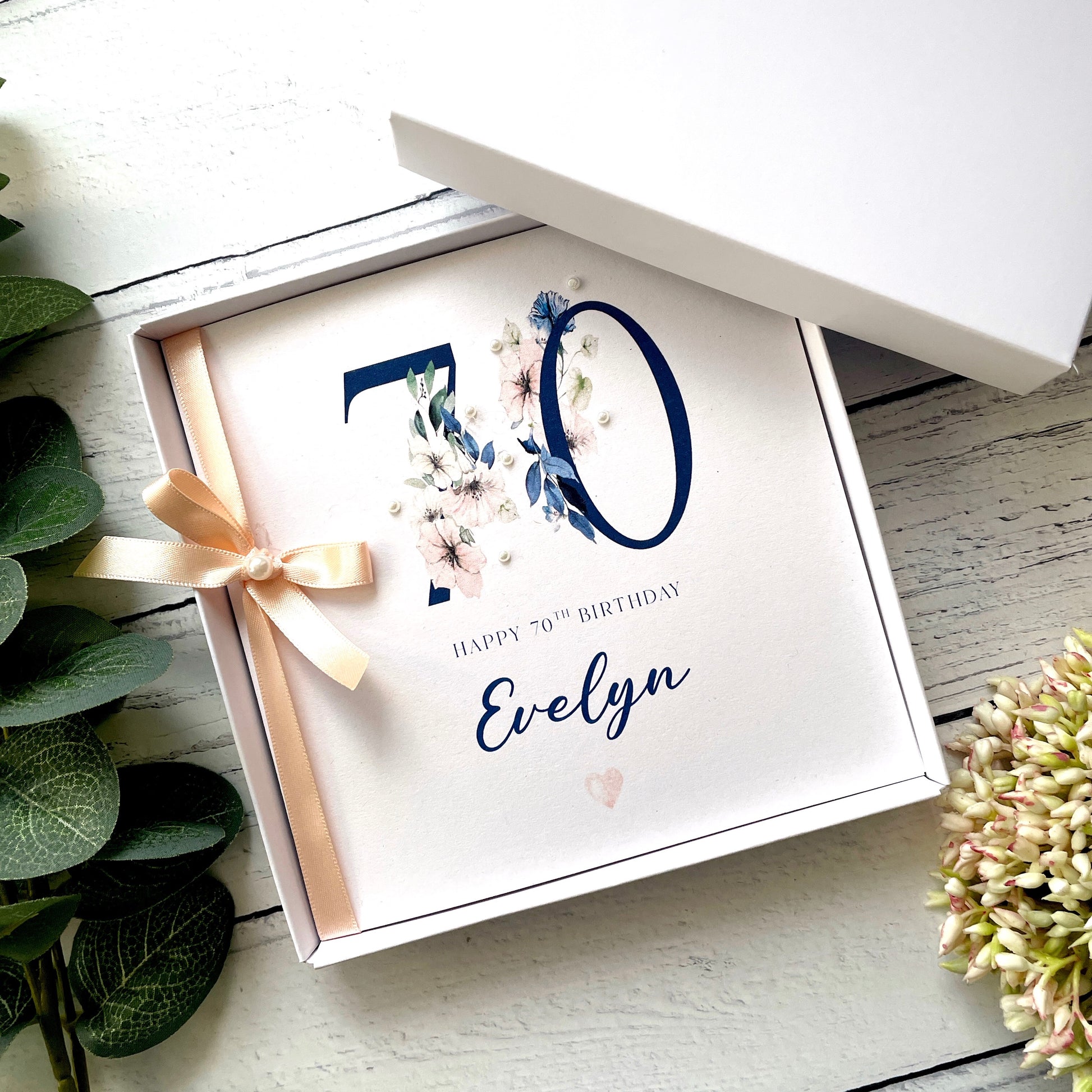 Gift box with a 'Happy 70th Birthday Evelyn' card on a wooden surface.