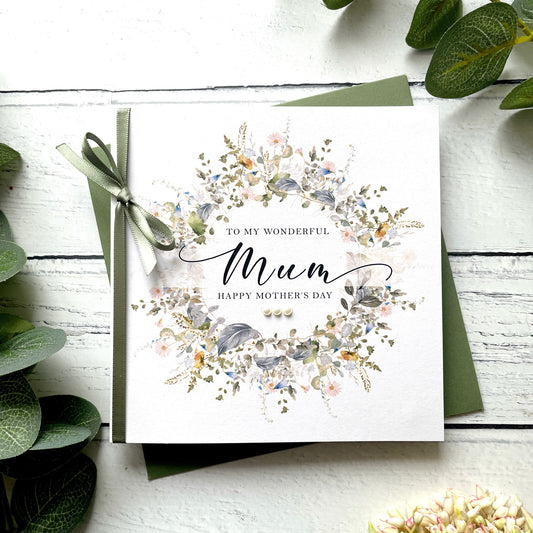 Greeting card for Mother's Day with floral design and ribbon on a white wooden surface.