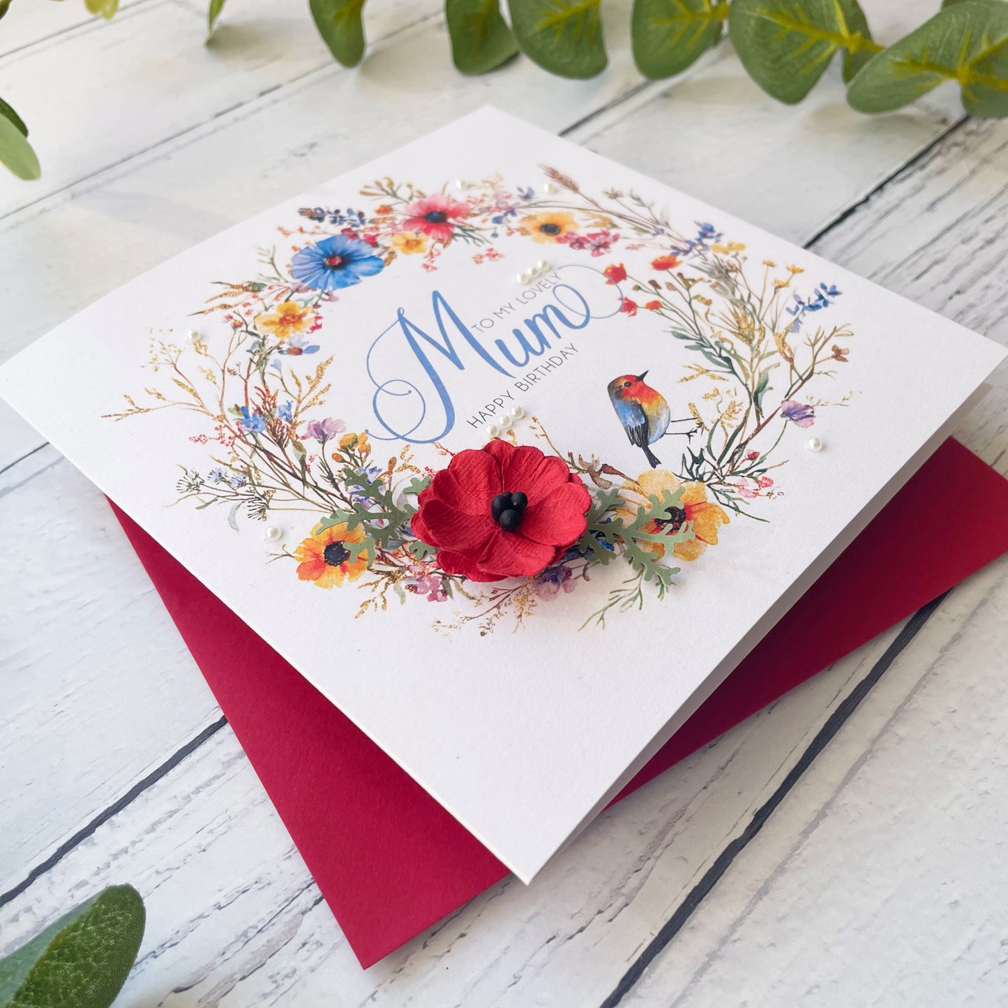 Greeting card with floral design and 'Happy Birthday Mum' text on a wooden surface.