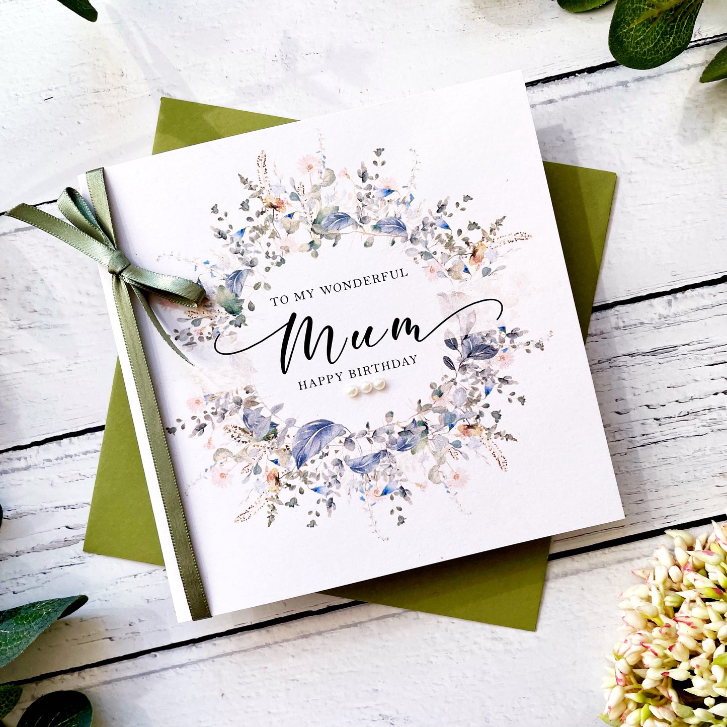 Greeting card for 'Mum' with floral design and green ribbon on a wooden surface