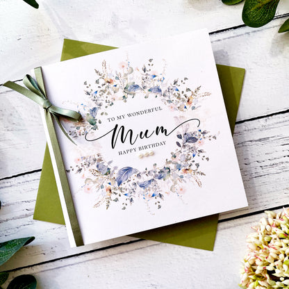 Greeting card for 'Mum' with floral design and green ribbon on a wooden surface