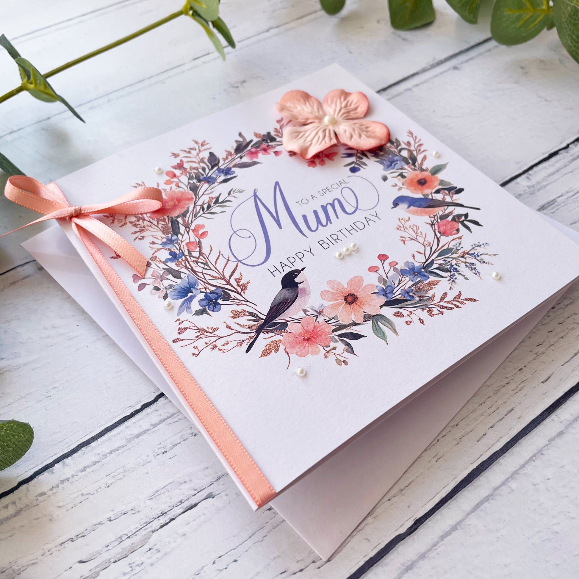 Greeting card with floral design and 'Happy Birthday Mum' text on a wooden surface.