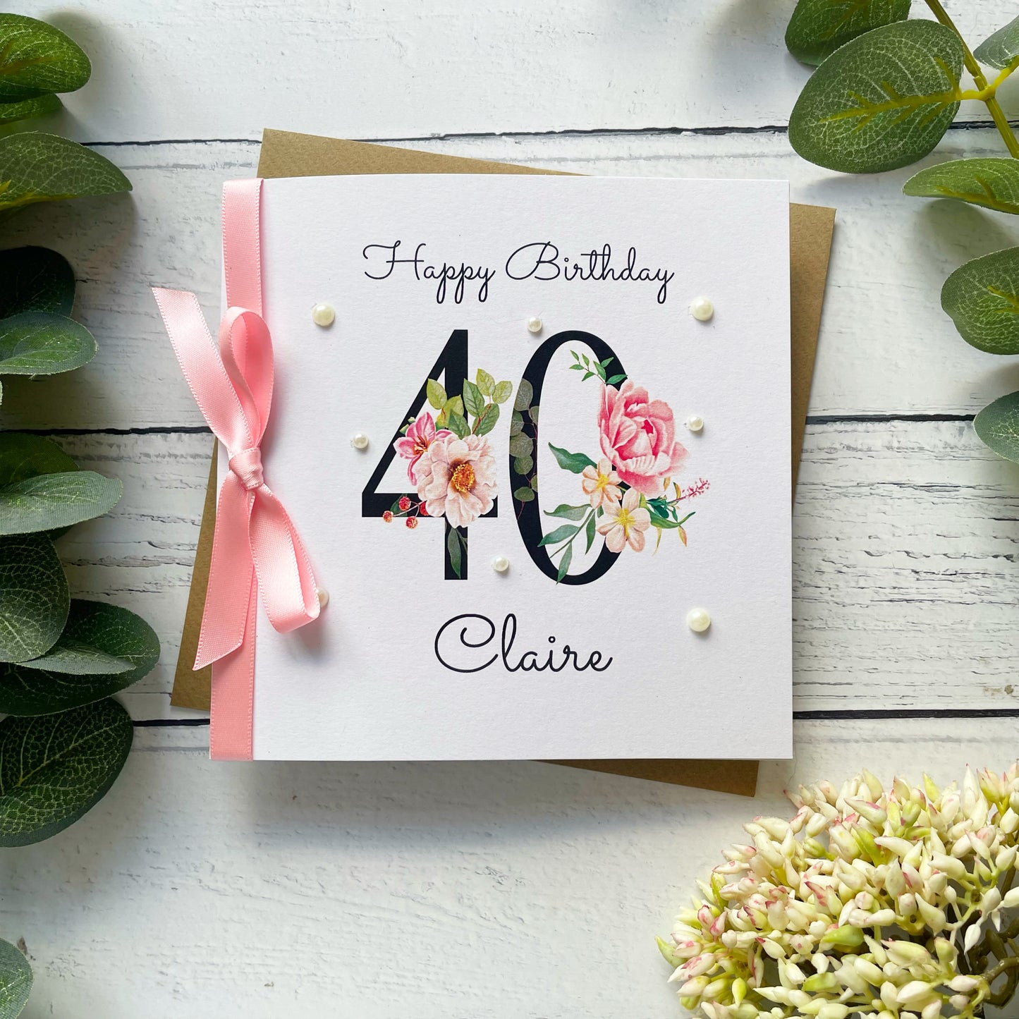Birthday card with floral design and number 40, featuring a pink ribbon on a white wooden background.