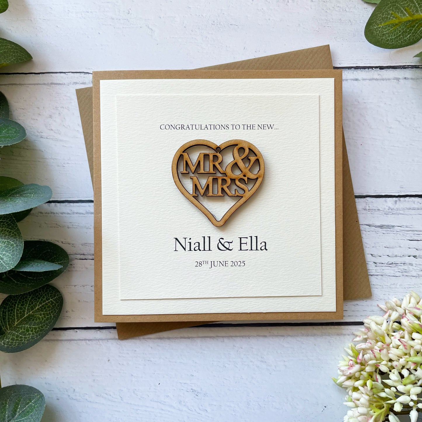 Wedding card with congratulations to the  new 'Mr & Mrs'  on a wooden heart design on a wooden surface with plants.