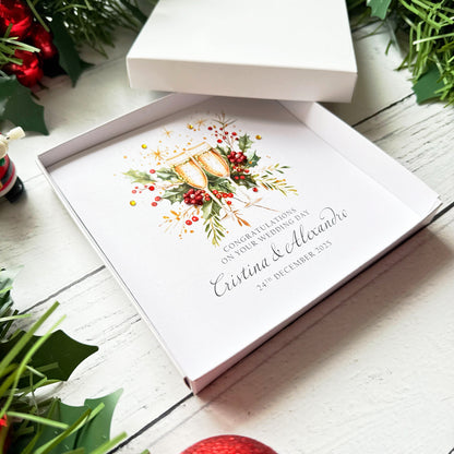 Christmas Wedding card with  festive floral design and text on a white box, surrounded by greenery and red flowers.