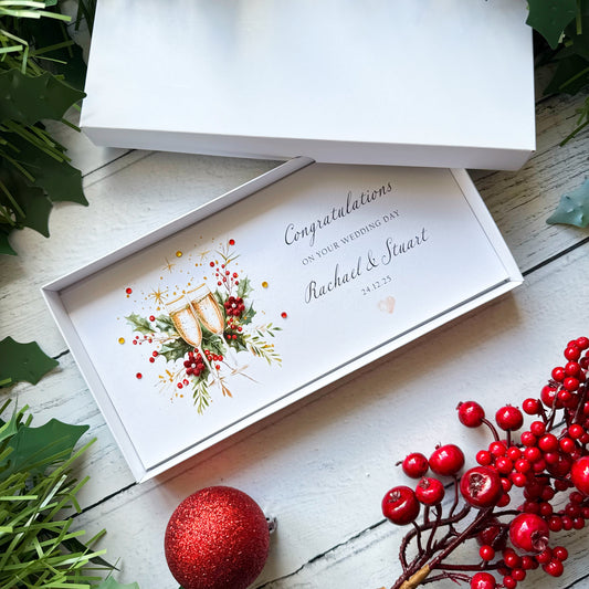Christmas wedding money wallet card with champagne flutes and berries in a decorative box, surrounded by festive elements on a wooden surface.