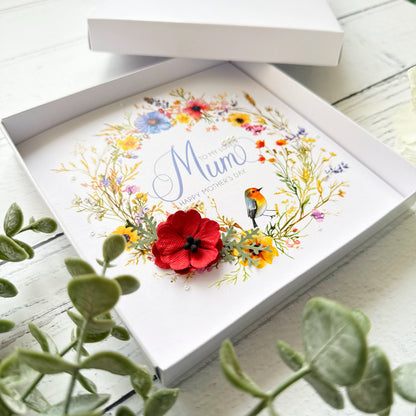 Greeting card with floral design and 'Mum' text, placed inside an open box on a wooden surface.