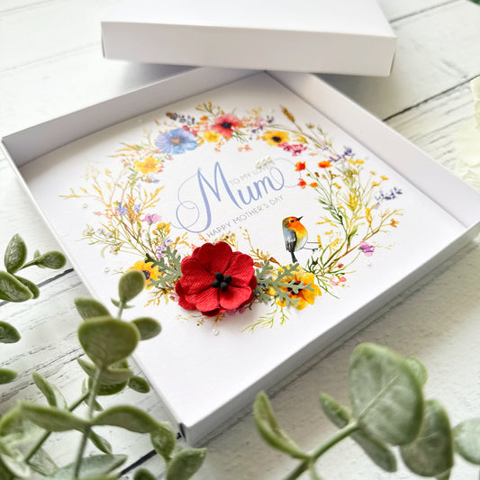 Greeting card with floral design and 'Mum' text, placed inside an open box on a wooden surface.