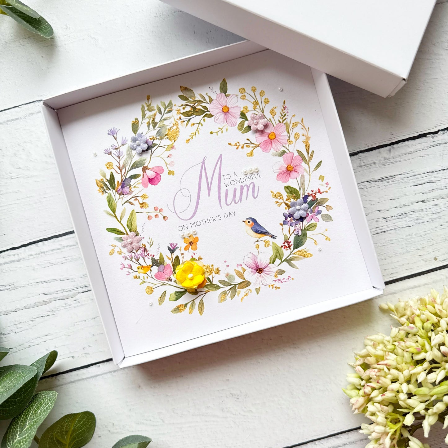 Mother's Day Greeting card with floral design and 'Mum' text in a box on a wooden surface.