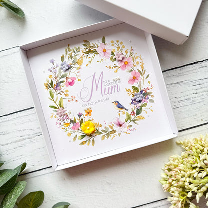 Mother's Day Greeting card with floral design and 'Mum' text in a box on a wooden surface.