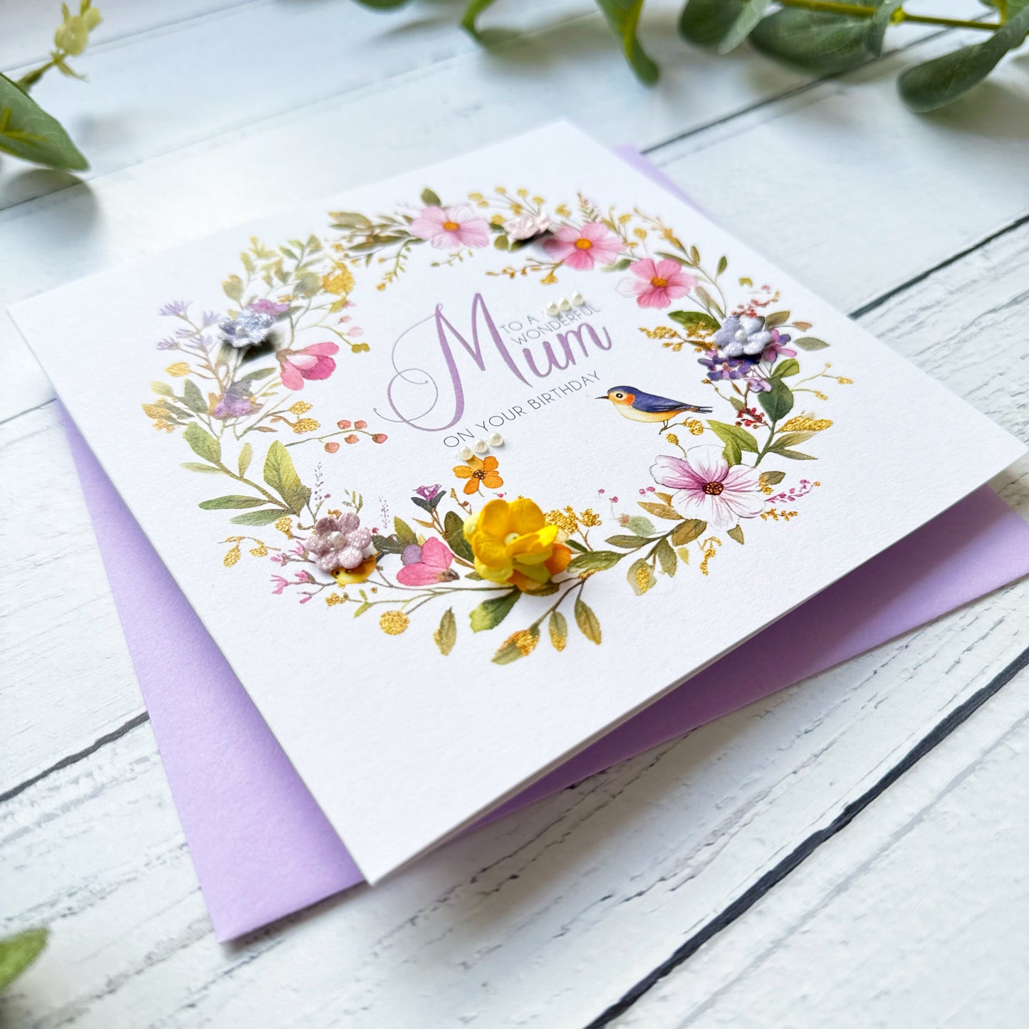 Greeting card with floral design and 'Happy Birthday Mum' text on a white wooden surface.