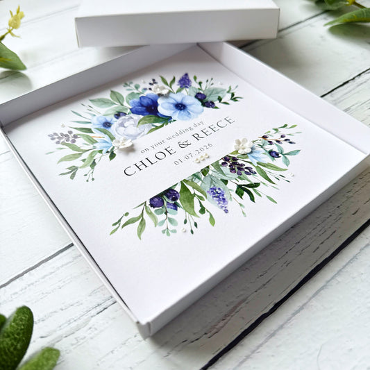 Wedding card with blue floral design and personalised text decorated with tiny pearls and paper flowers in a white box.