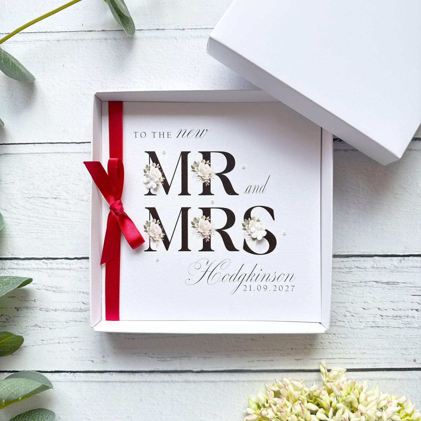 Wedding Card in a Gift box with 'Mr and Mrs' text and red ribbon on a white wooden surface