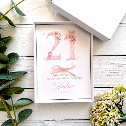 21st birthday card with floral design with a bow and pearls. With personalised text on a wooden surface with plants.
