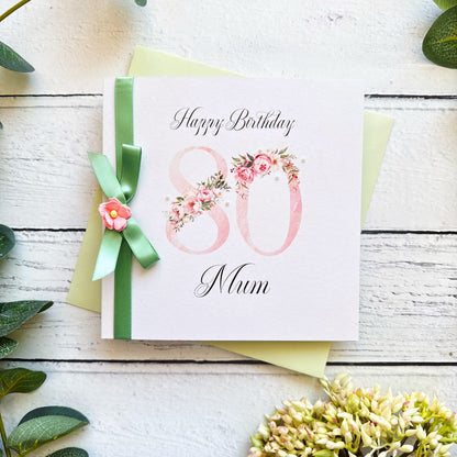 80th birthday card for mum with floral design and green ribbon on a wooden surface.