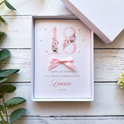 Personalised 18th birthday card with floral design and pink ribbon in a box on a wooden surface.