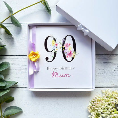 90th birthday Greeting card with 'Happy Birthday Mum'. Decorated with lilac ribbon yellow flower and pearls on a white wooden surface with decorative elements.