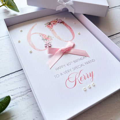 60th birthday greeting card with floral design with pink bow and pearls in a box. With personalised text on a wooden surface