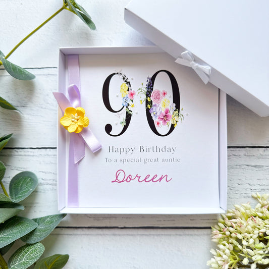 90th birthday greeting card with floral number design with a lilac bow, yellow flower and pearls. Personalised message on a white background