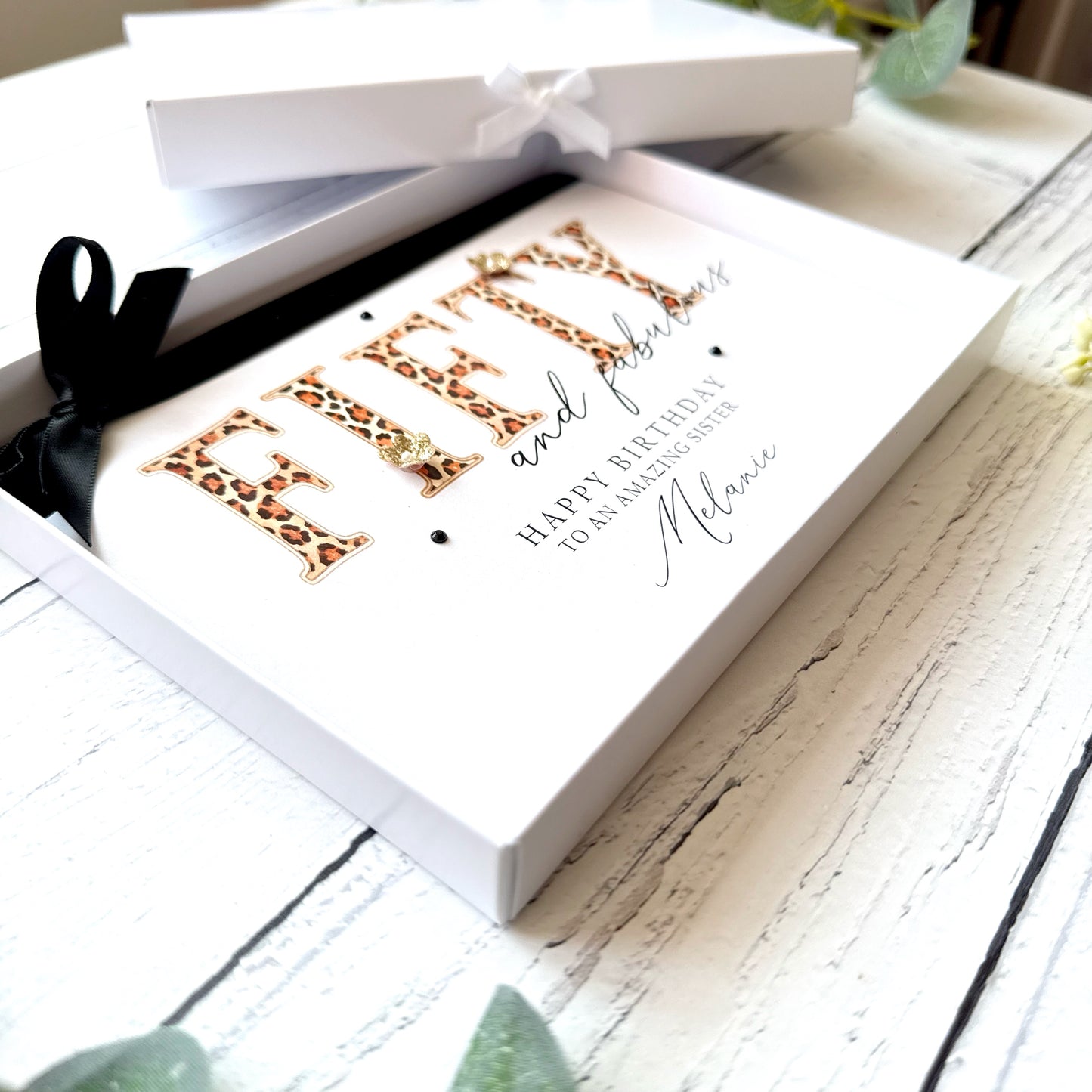 Greeting card with leopard print text "Fifty and Fabulous" 'Happy Birthday' in a white box on a wooden surface.