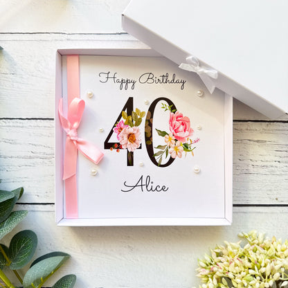 Personalised floral 40th birthday card for her featuring a large black number 40 decorated with pink roses and delicate flowers. The name Alice is printed beneath the number in elegant script. Hand-finished with a pink satin ribbon bow and pearl embellishments. Shown with a coordinating pink envelope and optional white presentation box.