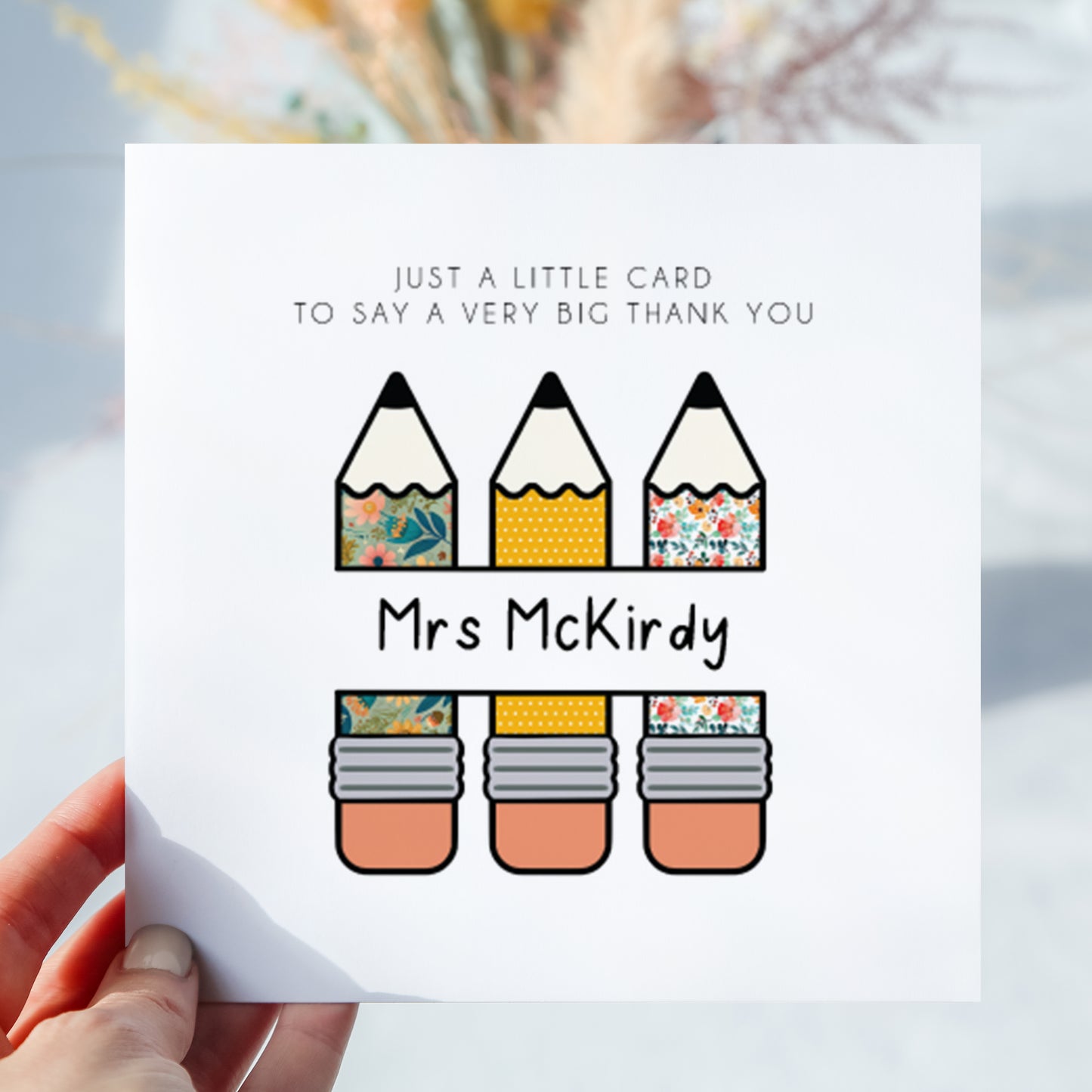 Personalised thank you teacher greeting card featuring three patterned pencil illustrations and the custom teacher name “Mrs McKirdy” across the centre. The card reads “Just a little card to say a very big thank you.” Displayed being held in hand against a softly blurred neutral background.