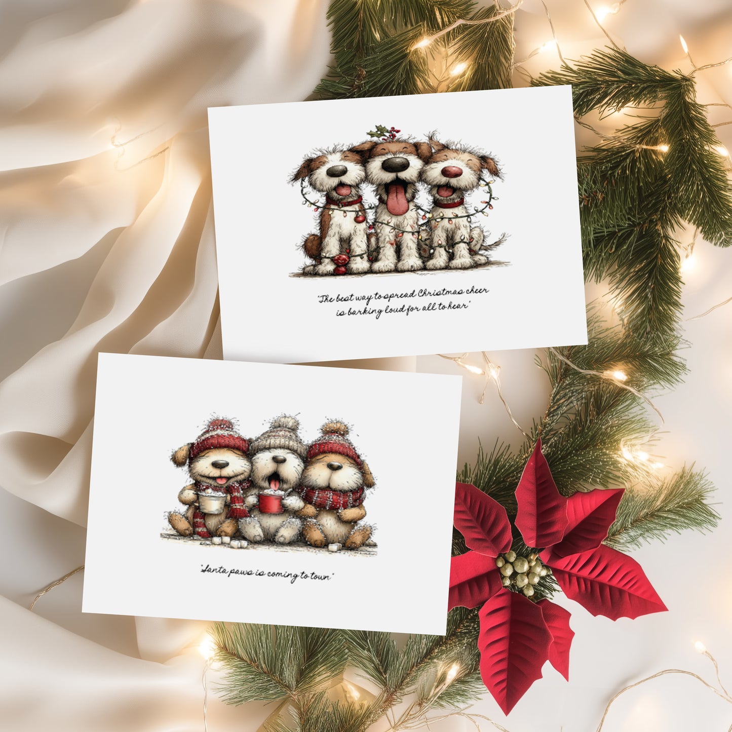 Two white Christmas cards featuring cute illustrated dogs. Card one shows three scruffy dogs tangled in fairy lights with the sentiment "The best way to spread Christmas cheer is barking loud for all to hear." Card two features three fluffy dogs in bobble hats and scarves holding hot chocolates with the sentiment "Santa paws is coming to town." Displayed on cream silk with pine branches and a red poinsettia.
