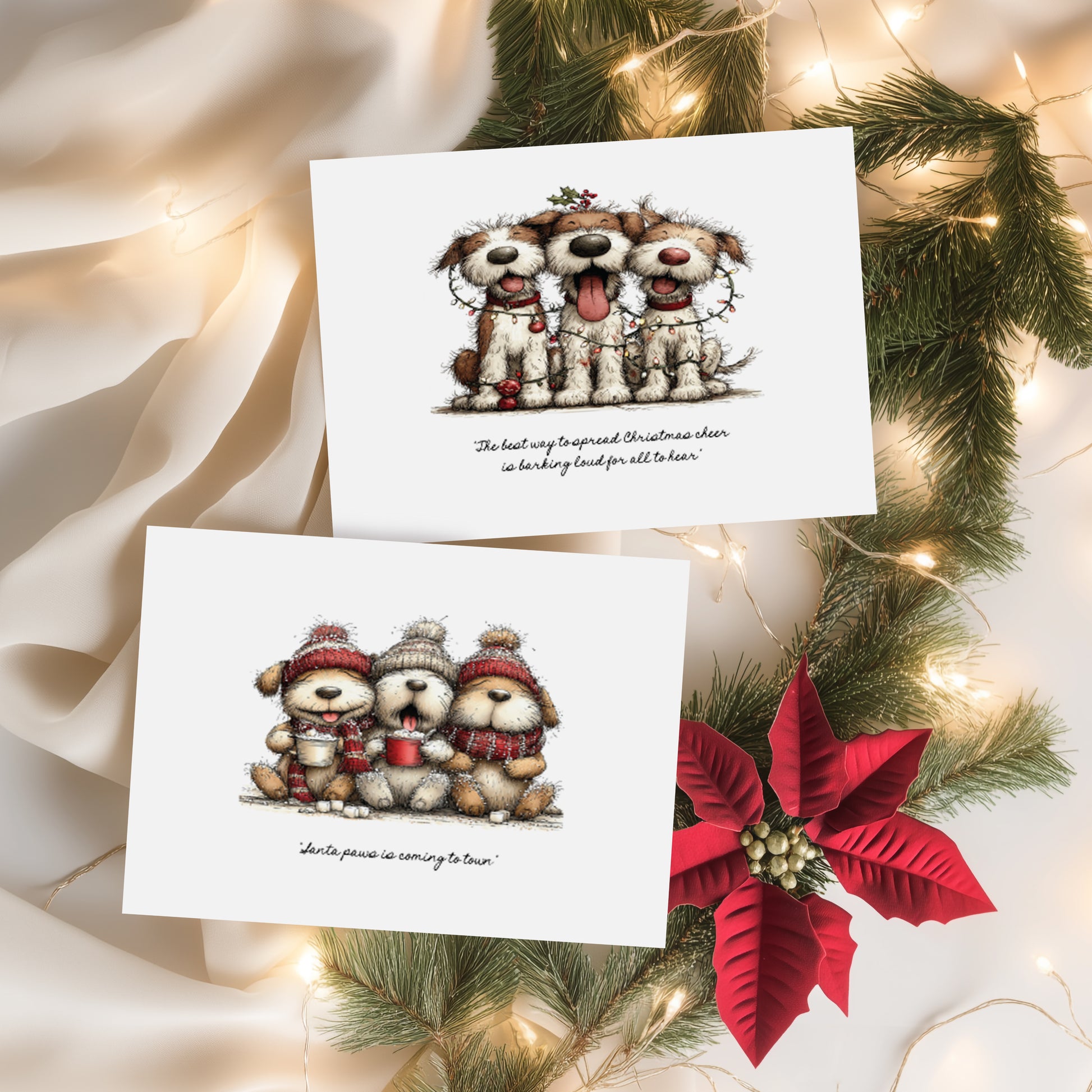 Two white Christmas cards featuring cute illustrated dogs. Card one shows three scruffy dogs tangled in fairy lights with the sentiment "The best way to spread Christmas cheer is barking loud for all to hear." Card two features three fluffy dogs in bobble hats and scarves holding hot chocolates with the sentiment "Santa paws is coming to town." Displayed on cream silk with pine branches and a red poinsettia.