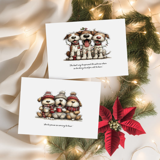 Two white Christmas cards featuring cute illustrated dogs. Card one shows three scruffy dogs tangled in fairy lights with the sentiment "The best way to spread Christmas cheer is barking loud for all to hear." Card two features three fluffy dogs in bobble hats and scarves holding hot chocolates with the sentiment "Santa paws is coming to town." Displayed on cream silk with pine branches and a red poinsettia.